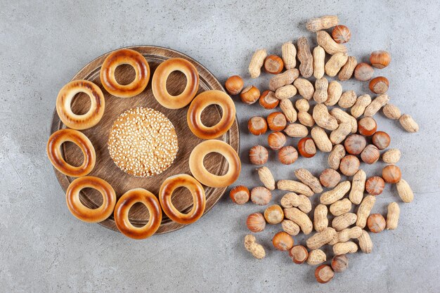 Enkel koekje omgeven door sushki op een houten bord naast verspreid assortiment noten op marmeren oppervlak.