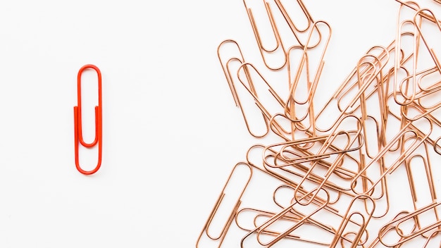 Enkele rode paperclip naast een stel koperen