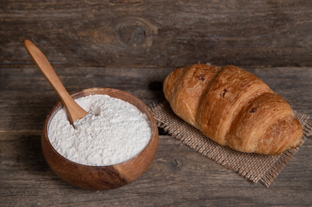 Enkele verse gewone croissant en kom met bloem houten oppervlak. Hoge kwaliteit foto