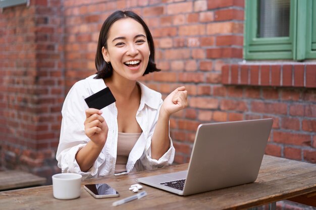 Enthousiast Aziatisch meisje zittend met creditcard en laptop betalen contactloos online winkelen via c