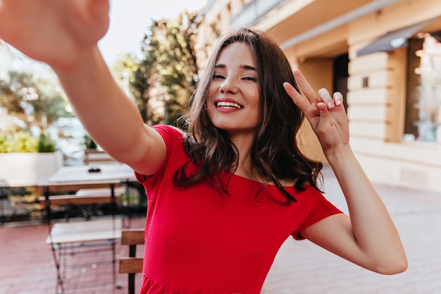 Enthousiaste blanke dame selfie maken op terras. Lachende debonair vrouw die een foto van zichzelf neemt.