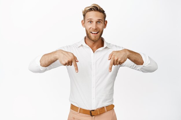 Enthousiaste blonde bebaarde man die lacht en met zijn vingers naar beneden wijst en een verkoopadvertentie toont die op een witte achtergrond staat