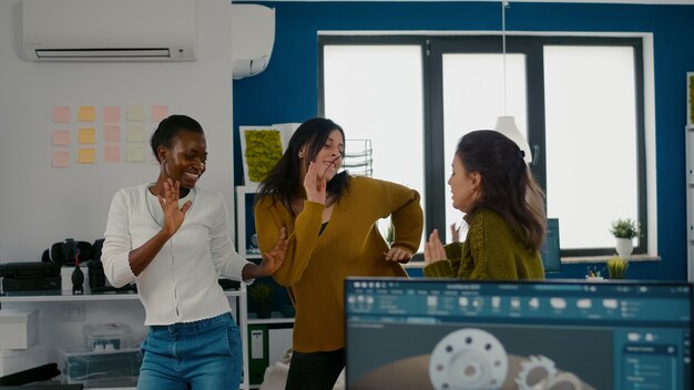 Enthousiaste diverse ingenieursvrouwen die dansen in het kantoor van het bedrijf en vieren het succes van de projectzang...