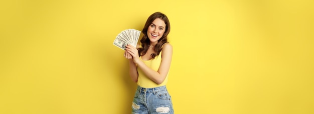 Enthousiaste glimlachende vrouw die geld contant laat lachen en er opgewonden uitziet terwijl ze in zomerkleding staat