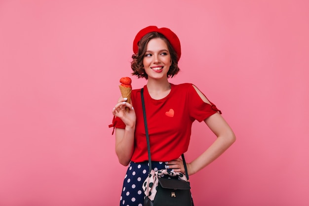 Enthousiaste jonge vrouw die in trendy kleding ijs eet. Binnenfoto van glimlachende onbezorgde dame met dessert.