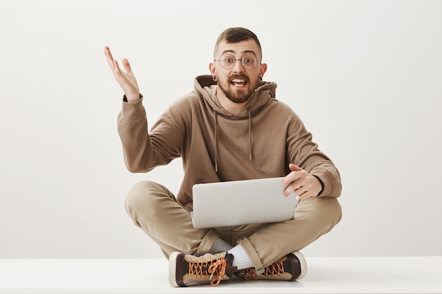 Enthousiaste man bespreekt iets zittend op gekruiste benen met laptop