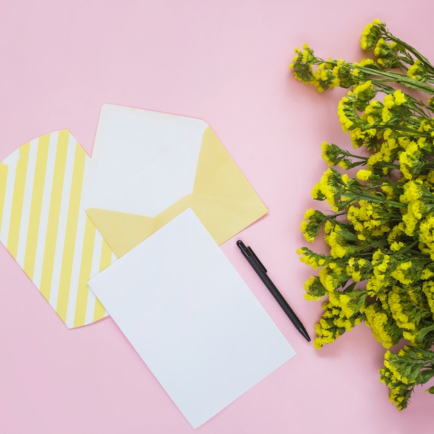 Gratis foto envelop; kaart; pen en gele bloem op roze achtergrond