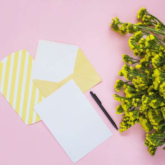 Envelop; kaart; pen en gele bloem op roze achtergrond