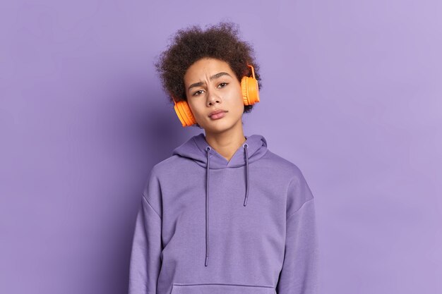 Ernstig Afrikaans-Amerikaans duizendjarig meisje luistert naar audiotrack via stereohoofdtelefoons heeft krullend, borstelig haar draagt een paarse hoodie.