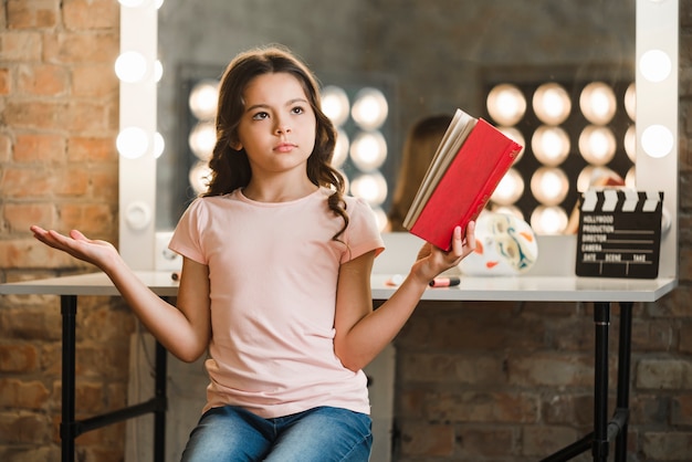 Gratis foto ernstig meisje die rood boek in haar hand het ophalen houden