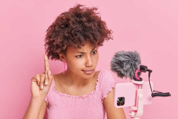 Gratis Foto ernstige attente afro-amerikaanse vrouw steekt wijsvinger op gericht op smartphonecamera heeft online gesprek met abonnees geeft belangrijke tips geïsoleerd over roze