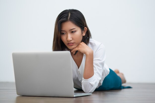 Ernstige Aziatische vrouw die op vloer met laptop