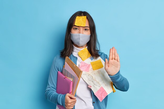 Ernstige brunette Aziatische vrouw kantoormedewerker houdt palm naar in stop gebaar, draagt een wegwerpmasker
