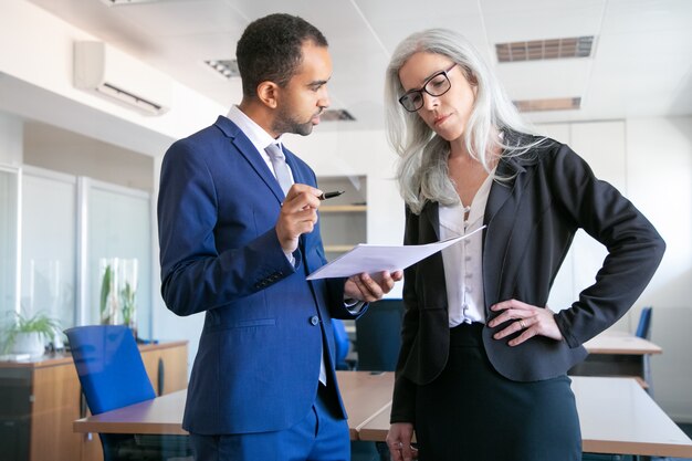 Ernstige collega's bespreken projectdocument voor ondertekening en vrouwelijke grijsharige manager in brillen luisterende baas. Partners die in vergaderruimte werken. Teamwork, bedrijfs- en managementconcept