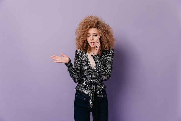 Ernstige dame in zwarte blouse met zilveren kralen praat aan de telefoon. Momentopname van jonge vrouw met blond krullend haar.