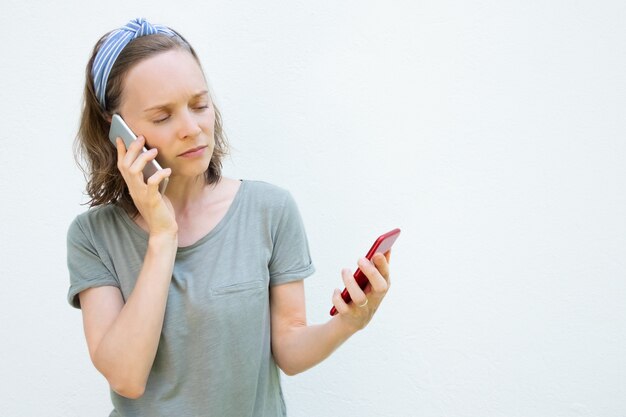 Ernstige drukke jonge vrouw met behulp van twee mobiele telefoons