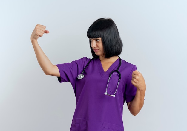 Ernstige jonge brunette vrouwelijke arts in uniform met stethoscoop