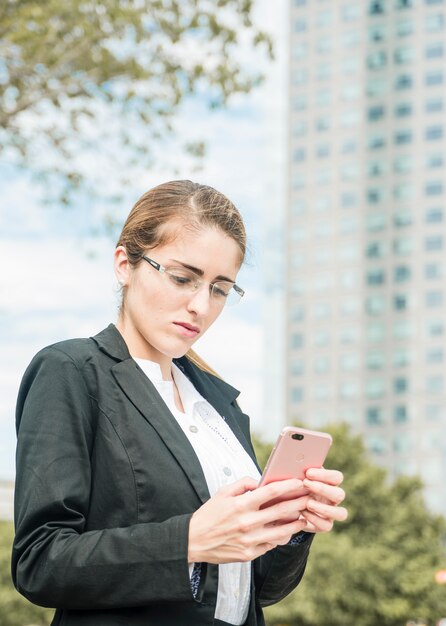 Ernstige jonge onderneemster die oogglazen draagt die mobiele telefoon met behulp van