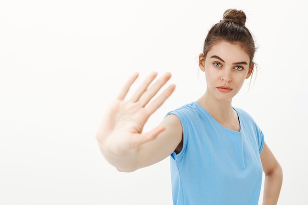 Ernstige jonge vrouw die zegt te stoppen, nee te zeggen, één hand uit te steken in een gebaar van verbod, waarschuwing of afkeuring