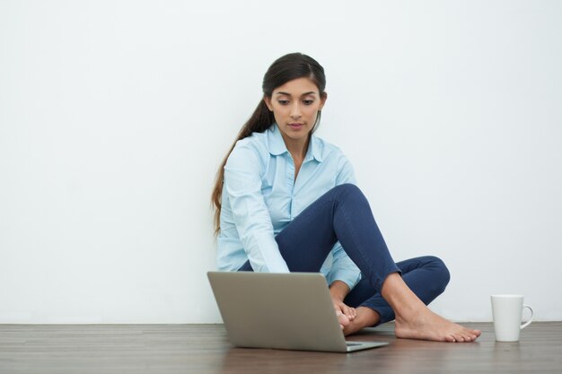 Ernstige Jonge vrouw met laptop en thee op Vloer