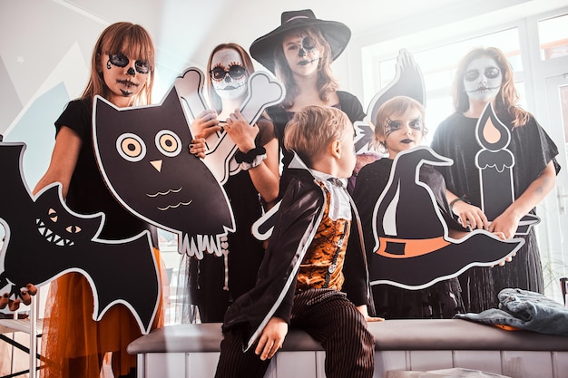 Ernstige kinderen in Halloween-kostuums poseren voor de fotograaf terwijl ze versieringen vasthouden.