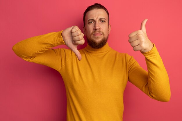 Ernstige knappe blonde man duimen omhoog en duim omlaag op roze