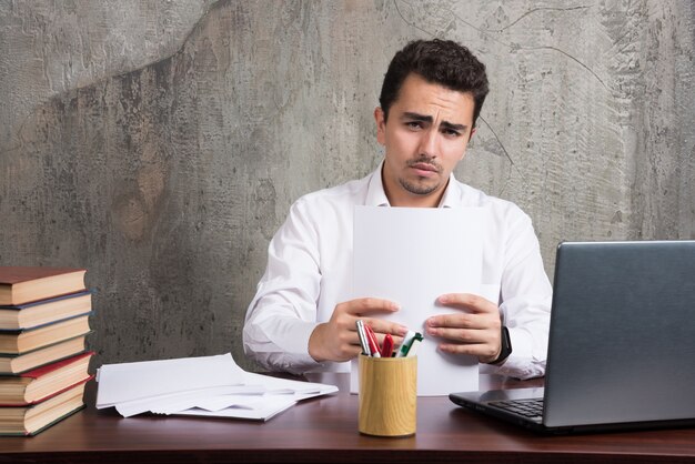 Ernstige man met vellen papier en zittend aan het bureau. Hoge kwaliteit foto