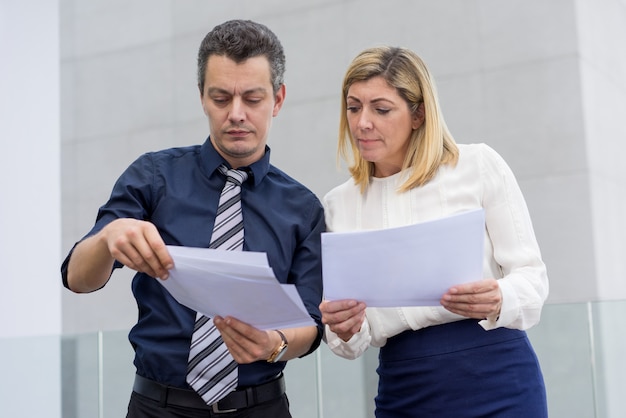 Ernstige mannelijke en vrouwelijke collega&#39;s die documenten in openlucht bespreken.