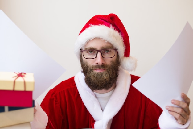 Gratis foto ernstige mens die het kostuum van de kerstman draagt en document opheft