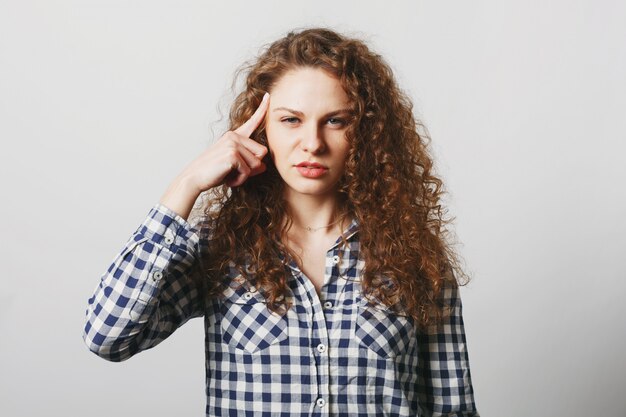 Ernstige mooie gekrulde vrouw houdt vinger op tempel terwijl ze probeert enkele details te onthouden