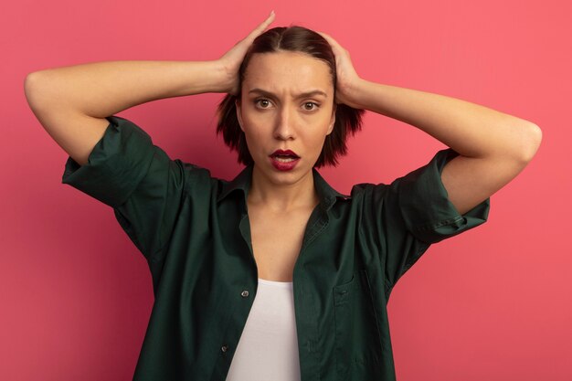 Ernstige mooie vrouw houdt hoofd geïsoleerd op roze muur