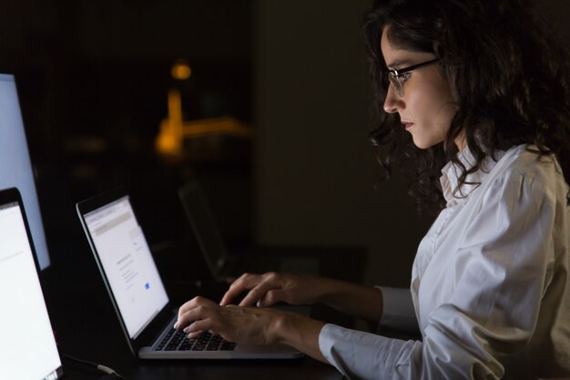 Ernstige onderneemster die laptop in donker bureau met behulp van