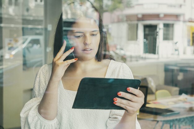 Ernstige onderneemster die op cel spreekt, tablet gebruikt en scherm bekijkt