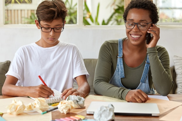 Gratis foto ernstige schooljongen in wit t-shirt, schrijft records in notitieblok, bezig met studeren