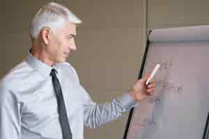 Gratis foto ernstige senior lecturer richten aan flipchart