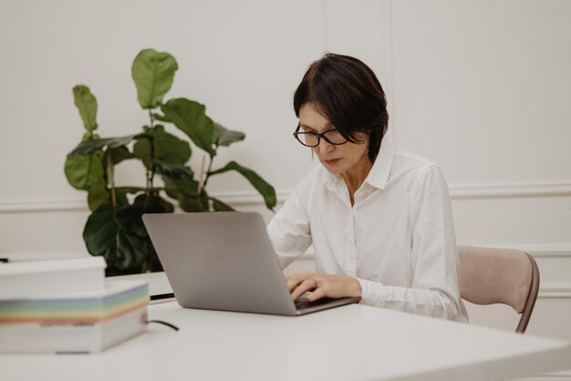 Ernstige volwassen Europese vrouw die computer gebruikt, beantwoordt e-mail terwijl ze aan tafel zit Freelance werk bedrijfsmensenconcept