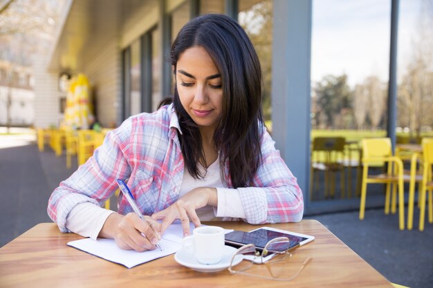 Ernstige vrouw die nota&#39;s in openluchtkoffie maakt