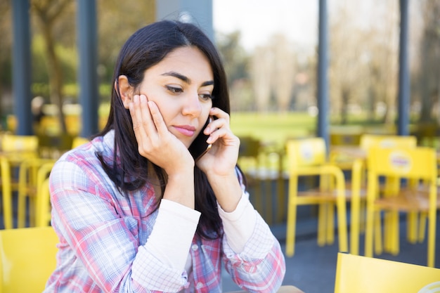 Ernstige vrouw die op mobiele telefoon in openluchtkoffie spreekt