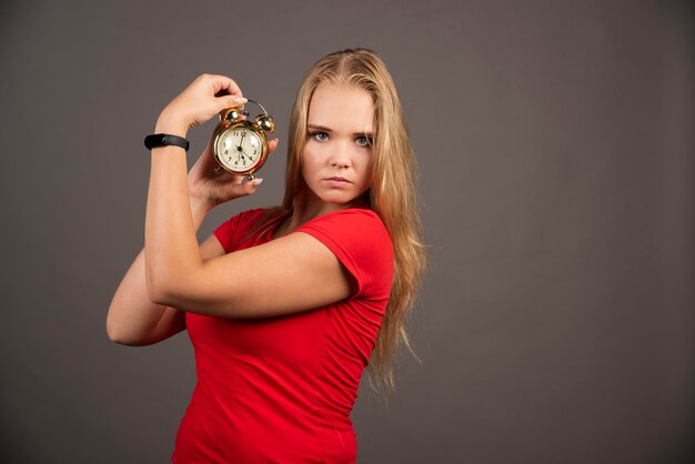 Ernstige vrouw die zich op zwarte muur met klok bevindt.