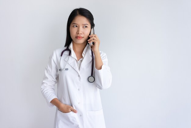 Ernstige vrouwelijke arts die op smartphone spreekt
