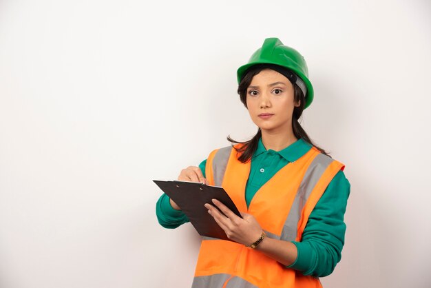 Ernstige vrouwelijke industrieel ingenieur in uniform met klembord op witte achtergrond.