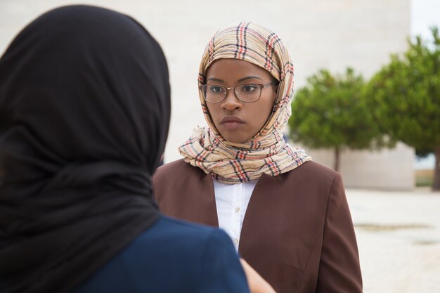 Ernstige vrouwelijke moslimvrouw praten met collega