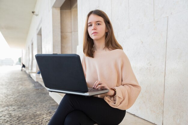 Ernstige vrouwelijke tiener die op laptop op bank doorbladert