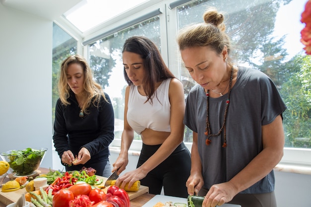 Ernstige vrouwen die groenten in keuken koken en snijden