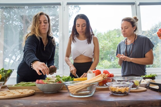 Ernstige vrouwen die groenten koken bij keukenlijst