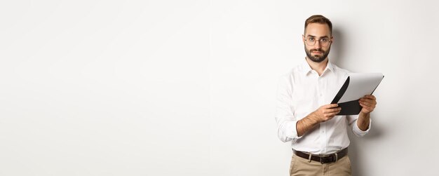 Ernstige werkgever die naar de camera kijkt tijdens het lezen van documenten op het klembord met sollicitatiegesprek standin