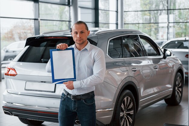 Ernstige zakenman. Manager staat voor moderne zilverkleurige auto met papier en documenten in handen