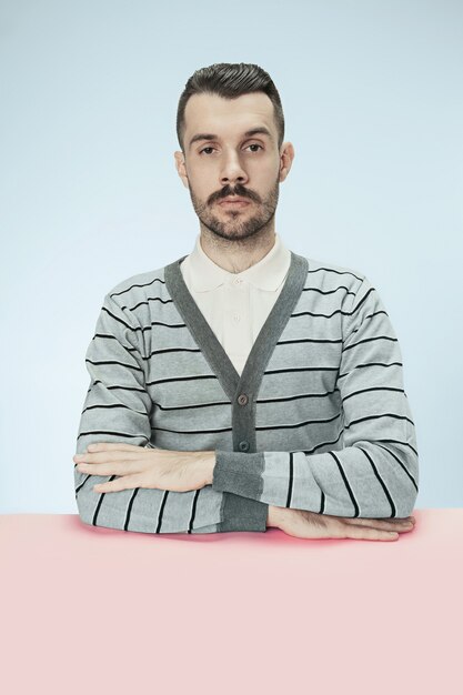 Ernstige zakenman zittend aan tafel op blauwe studio achtergrond. Het portret in minimalistische stijl