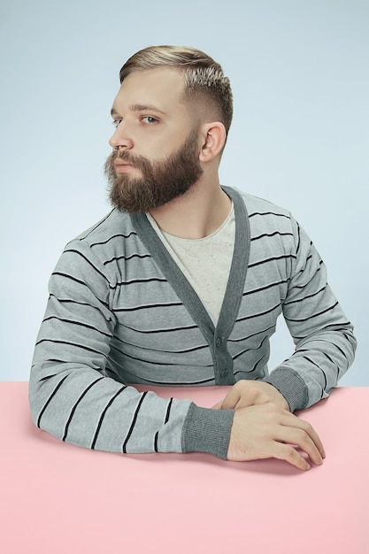 Ernstige zakenman zittend aan tafel op blauwe studio achtergrond. Het portret in minimalistische stijl