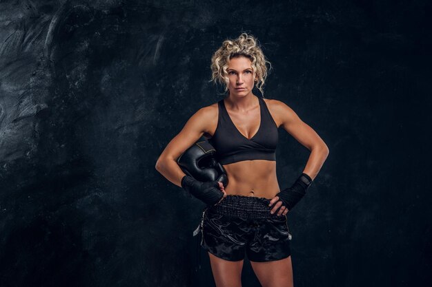 Ervaren vrouwelijke bokser poseert voor fotograaf in donkere fotostudio met apparatuur in haar handen.